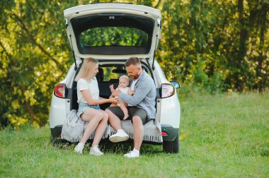 Genç bir aile. Beyaz elbiseli üç kişi piknik yapıyor. Güzel ebeveynler ve kızlar yaz tatilinde arabayla seyahat ederler. Parkta Sahne