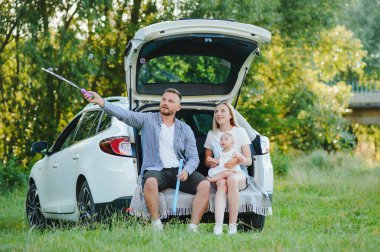 Genç bir aile. Beyaz elbiseli üç kişi piknik yapıyor. Güzel ebeveynler ve kızlar yaz tatilinde arabayla seyahat ederler. Parkta Sahne