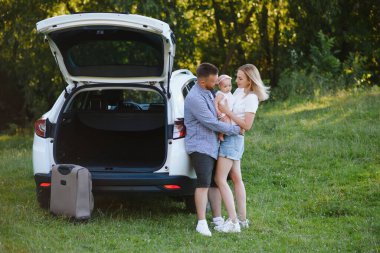 Genç bir aile. Beyaz elbiseli üç kişi piknik yapıyor. Güzel ebeveynler ve kızlar yaz tatilinde arabayla seyahat ederler. Parkta Sahne