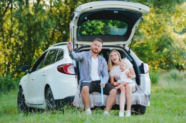 Genç bir aile. Beyaz elbiseli üç kişi piknik yapıyor. Güzel ebeveynler ve kızlar yaz tatilinde arabayla seyahat ederler. Parkta Sahne