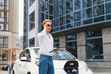 Yakışıklı bir genç adam modern elektrikli arabasını şarj ediyor..