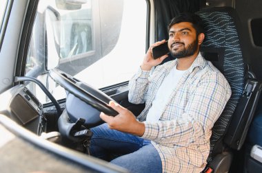 Hintli bir adam ağır bir kamyon kullanıyor, akıllı bir telefonla konuşuyor, ulaşımda iletişim ve lojistiği temsil ediyor.