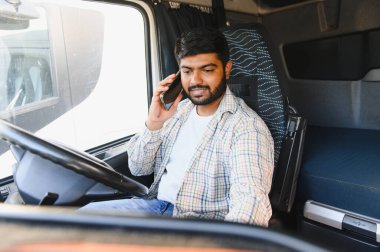 Genç bir adam kamyonet kullanıyor, akıllı telefonla konuşuyor, lojistik ve ulaşımla bağlantı kuruyor.