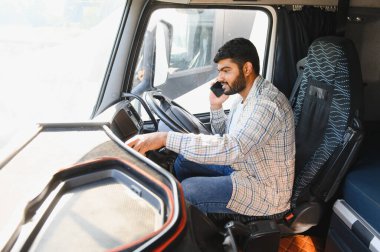 Erkek kamyon şoförü akıllı telefondan iletişim kuruyor. Kamyon kabininde oturuyor, nakliye lojistiği yönetiyor.