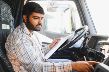 Hintli kamyon şoförü kulübede evrak işleriyle uğraşıyor, kamyonculuk ve lojistiğe odaklanıyor.