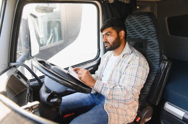Erkek Hintli kamyon şoförü bir kamyonda oturuyor, bir panoya yazı yazıyor, teslimat evraklarını tamamlıyor.