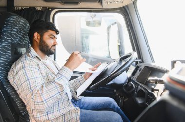 Kamyon kabininde önemli belgeleri tamamlayan adam teslimat ve ulaşım yönetimine odaklanıyor.