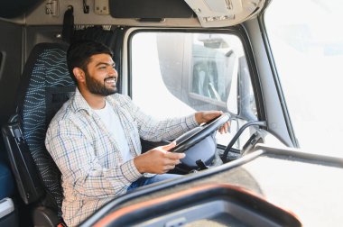 Gülümseyen Hintli erkek kamyon şoförü ağır aracını kullanıyor, malları lojistik ve teslimat yoluyla taşıyor.