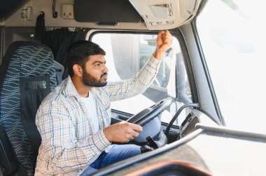 Genç Hintli bir adam büyük bir kamyon kullanıyor, ön camdan içeri bakıyor, profesyonel nakliye işine odaklanmış.