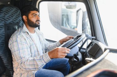 Bir kamyonun direksiyonundaki genç adam, yola odaklanmış, ulaşım ve lojistik işleri yapıyor.