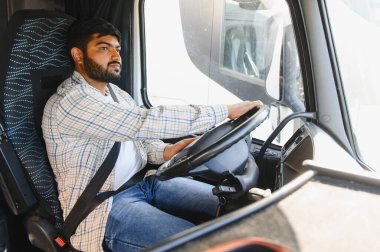 Büyük bir ticari kamyon süren Hintli adam, önündeki yola odaklanıyor. Lojistik işleri için mal taşıma