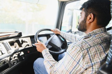 Yarı kamyon süren Hintli bir adam, yolculuk sırasında yola odaklanıyor, lojistik ve ulaşım endüstrisini temsil ediyor.