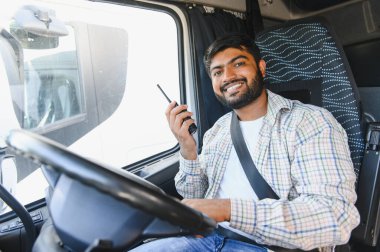 Takside gülümseyen Hintli kamyon şoförü elinde telsiz, kendinden emin profesyonel uzun mesafe taşımaya ve lojistik görevlerine hazır.