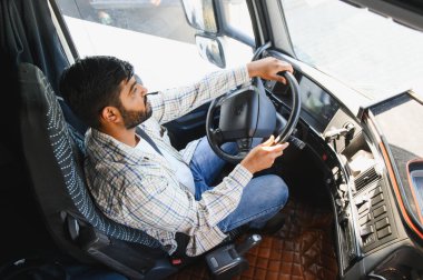Profesyonel bir erkek sürücü ticari bir kamyon kullanıyor, yola odaklanıyor ve direksiyonu tutuyor.