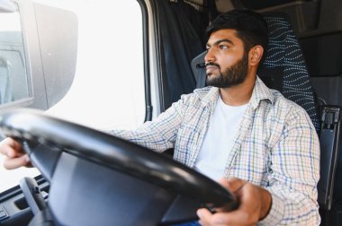 Genç Hintli adam ticari kamyon kullanıyor. Ekose gömlek giyerek yola odaklanmış. Profesyonel ulaşım işçisi.