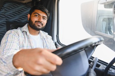 Ticari kamyon süren Hintli bir adam, kameraya bakıyor, profesyonelliği, lojistiği ve ulaşımı aktarıyor.