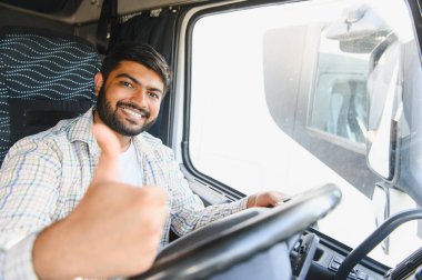 Kamyon kabinindeki Hintli adam başparmağını kaldırıyor, gülümsüyor ve kameraya bakıyor. Ulaştırma ve dağıtım hizmetlerini temsil ediyorum.