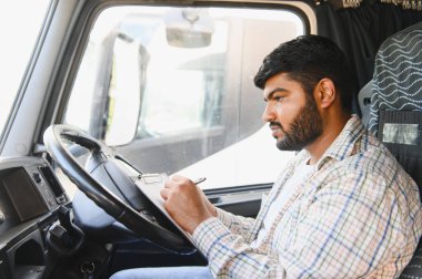 Minibüsün içindeki Hintli adam bir panoya yazı yazıyor, nakliye ve kargo teslimatı için gerekli evrakları tamamlıyor.