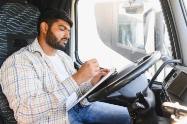 Kamyon şoförü bir panoya yazı yazıyor. Araç kabinindeki ulaşım ve lojistik belgelerini yönetiyor.