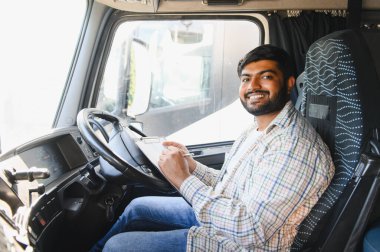 Minibüste oturan gülümseyen Hintli erkek kamyon şoförü elinde bir pano ve kalemle kameraya bakıyordu.