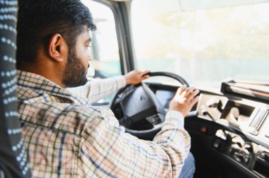Ekose gömlekli Hintli bir adam ticari bir kamyon kullanıyor, önündeki yola odaklanıyor. Taşımacılık ve lojistik işi