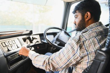 Ticari kamyon süren Hintli bir adam, torpido gözündeki kontrolleri ayarlıyor. Ulaşım, lojistik ve teslimatı temsil ediyor.