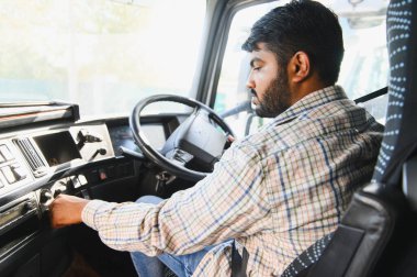 Ekose gömlekli Hintli adam anahtarı kontağa çeviriyor. Kamyon kabininde nakliye işine hazırlanıyor.