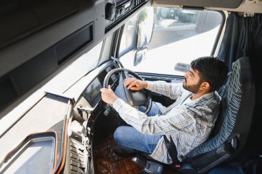 Adam direksiyona odaklanmış, uzun bir nakliye yolculuğu sırasında otoyolda yarı kamyon kullanıyor, profesyonel bir şoför iş başında.