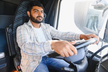 Genç Hintli adam ticari kamyon kullanıyor, önündeki yola odaklanıyor. Nakliye sektöründe çalışan profesyonel bir erkek kamyon şoförü.