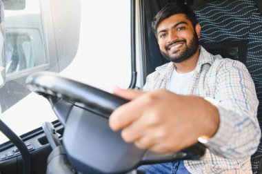 Ticari bir araç kullanan Hintli bir sürücü, sıradan bir tişört giyiyor ve gülümsüyor, lojistik ve taşımayı temsil ediyor.