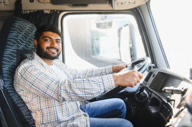 Genç Hintli kamyon şoförü gülümsüyor, şoför koltuğundan bir tırı sürüyor, ulaşım ve lojistiği temsil ediyor.