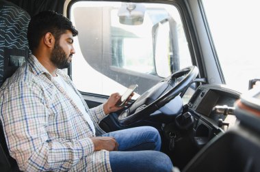 Taksideki genç kamyon şoförü, uzun mesafe teslimat sırasında kamyonda park halindeyken akıllı telefonu kontrol ediyor.