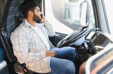 Erkek kamyon şoförü akıllı telefondan iletişim kuruyor, bir araç kulübesinde oturuyor. Lojistiği yönetiyor ya da bağlantıda kalıyor.