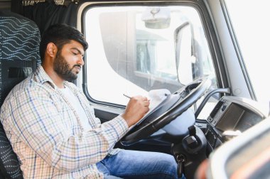 Taksideki Hintli kamyon şoförü evrakları dolduruyor ve panoya çek yazıyor. Lojistik, nakliye ve nakliye işleriyle uğraşıyor.