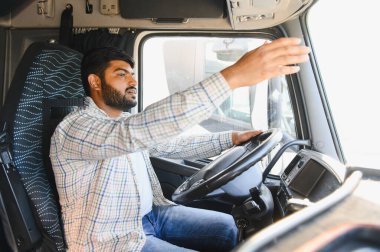 Hintli adam ağır bir araç kullanıyor, yola odaklanıyor. Lojistik, ulaşım ve nakliye endüstrilerini temsil ediyor.