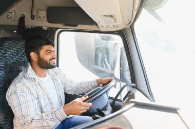 Hintli adam ağır bir araç kullanıyor, gülümsüyor ve ileriye bakıyor. Ulaşım sektöründe çalışan profesyonel bir sürücü.