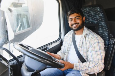 Hintli erkek kamyon şoförü gülümsüyor, aracının kabininde oturuyor. Lojistik şirketleri için mal taşıma