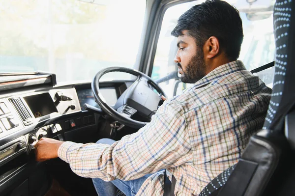 Ekose gömlekli Hintli adam anahtarı kontağa çeviriyor. Kamyon kabininde nakliye işine hazırlanıyor.