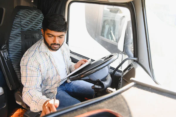Araç taksisinde evrak dolduran bir adam, karayolu yolculuğuna başlamadan önce lojistik belgelerini yönetiyor.