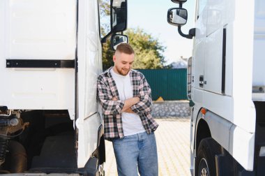 İki büyük beyaz kamyonun arasında kolları çapraz duran gülümseyen genç adam. Ulaşım ve lojistik kavramı