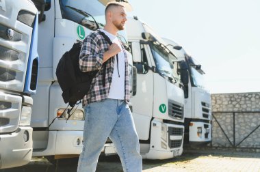 Öğrenci sembolleri taşıyan kamyonların yanından geçen sırt çantalı genç bir adam. Lojistik, ulaşım ve yeni bir kariyer yolu sunuyorum.