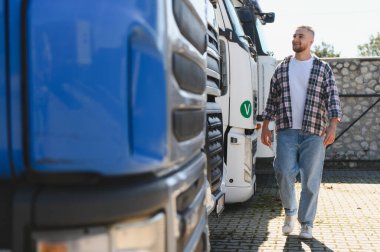 Ağır kargo kamyonlarının yanından geçen adam ulaşım endüstrisini, lojistiği ve profesyonel kariyer yollarını temsil ediyor.