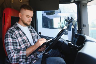 Lojistik belgeleri dolduran bir adam, kamyon kabininden sorunsuz ulaşım ve teslimat operasyonları sağlıyor.