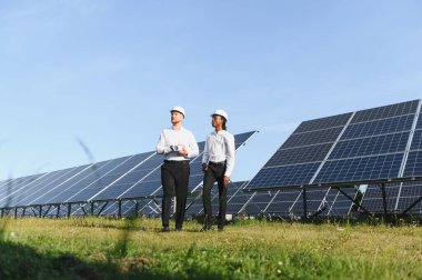 Temiz enerji ve sürdürülebilirliğe odaklanmış, yürüyen ve büyük bir güneş enerjisi santralini izleyen iki farklı mühendis.