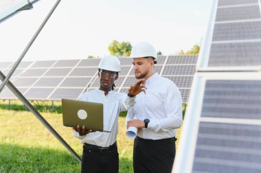 Bir enerji santralinde sürdürülebilir teknoloji geliştirmeyi güvence altına alan güneş enerjisi projesini tartışan iki mühendis bir dizüstü bilgisayar kullanıyor.