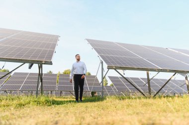 Bir güneş çiftliğinde güvenle yürüyen iş adamı yenilenebilir enerji, yeşil enerji ve sürdürülebilir iş gelişimini sembolize ediyor