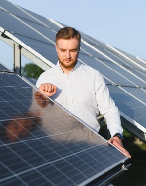 Adam güneş panelini kontrol ediyor. Açık havada yenilenebilir enerji, sürdürülebilirlik ve temiz teknolojiyi temsil ediyor.