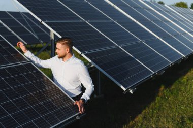 Bir güneş çiftliğindeki güneş panellerini denetleyen genç erkek mühendis, temiz, verimli yenilenebilir enerji gelişimi performansını izliyor