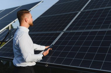 Genç mühendis tablet kullanarak güneş panelleri enerji üretimini kontrol ediyor. Yeşil enerji kavramı ve sürdürülebilir teknoloji