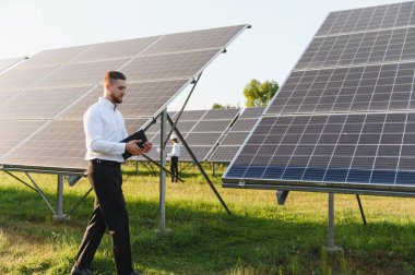 Güneş çiftliğinde elinde bir tabletle yürüyen ve güneş panellerini inceleyen bir mühendis. Yenilenebilir enerji ve temiz teknolojinin vurgulanması